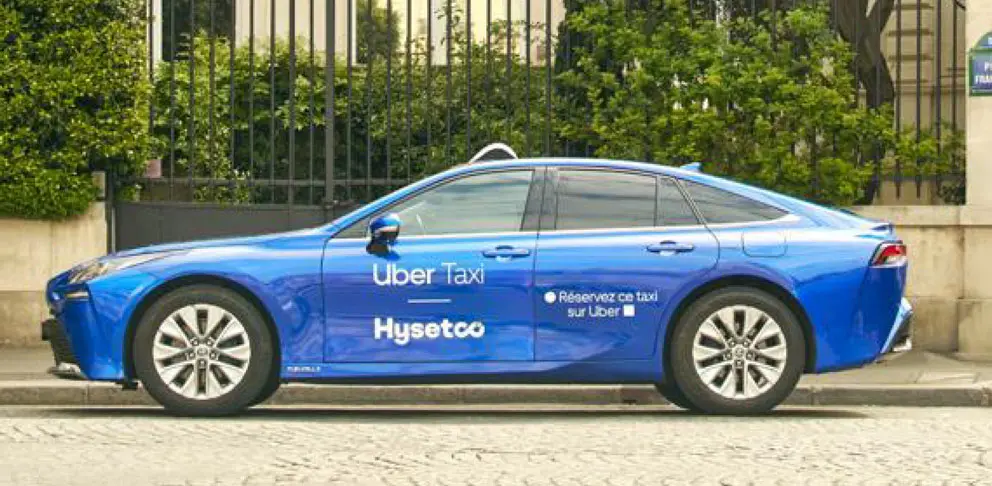 Blue Uber taxi sedan parked on a city street with 'Uber Taxi' and 'Hysetco' branding on the side, side-profile view.